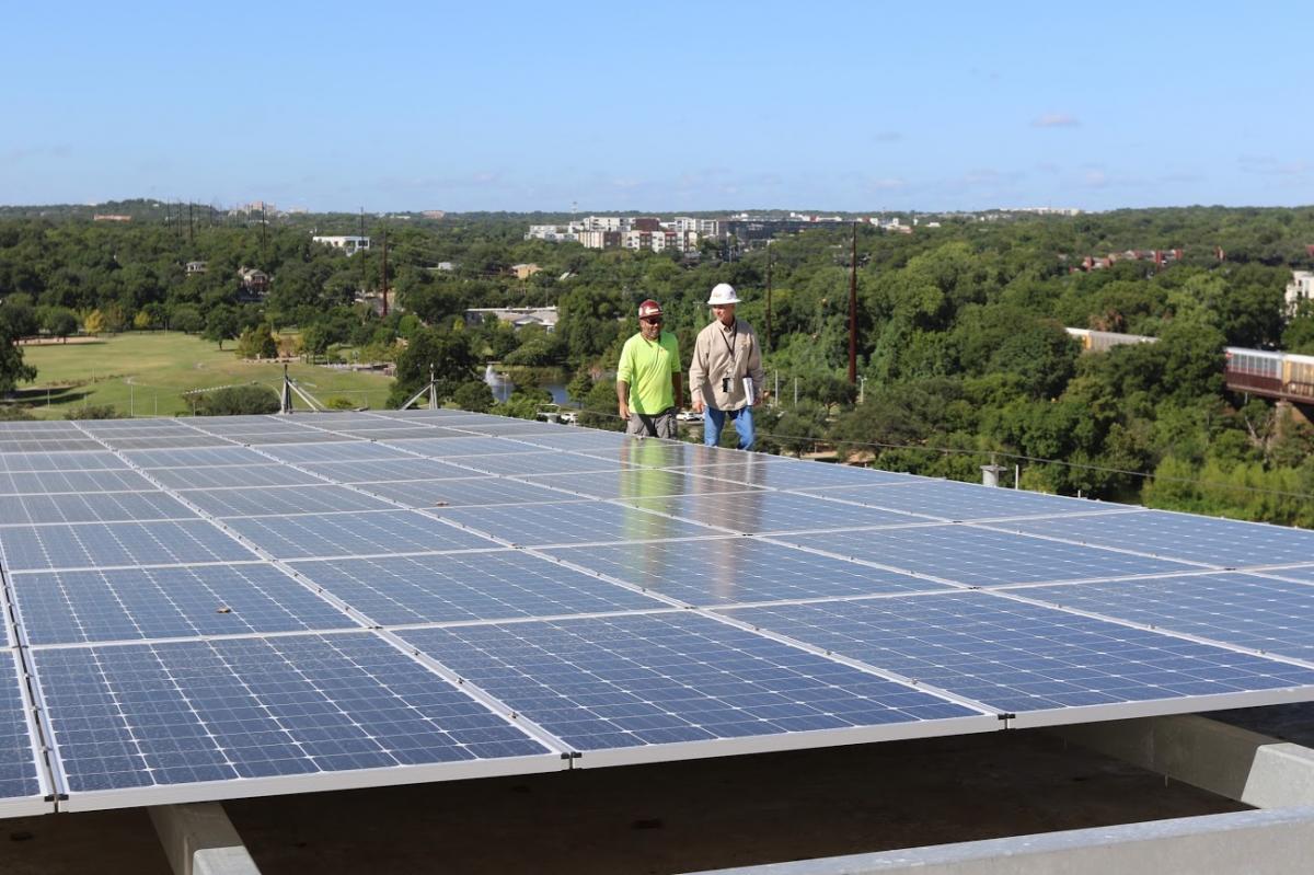 Two workers behind solar panels with trees in background